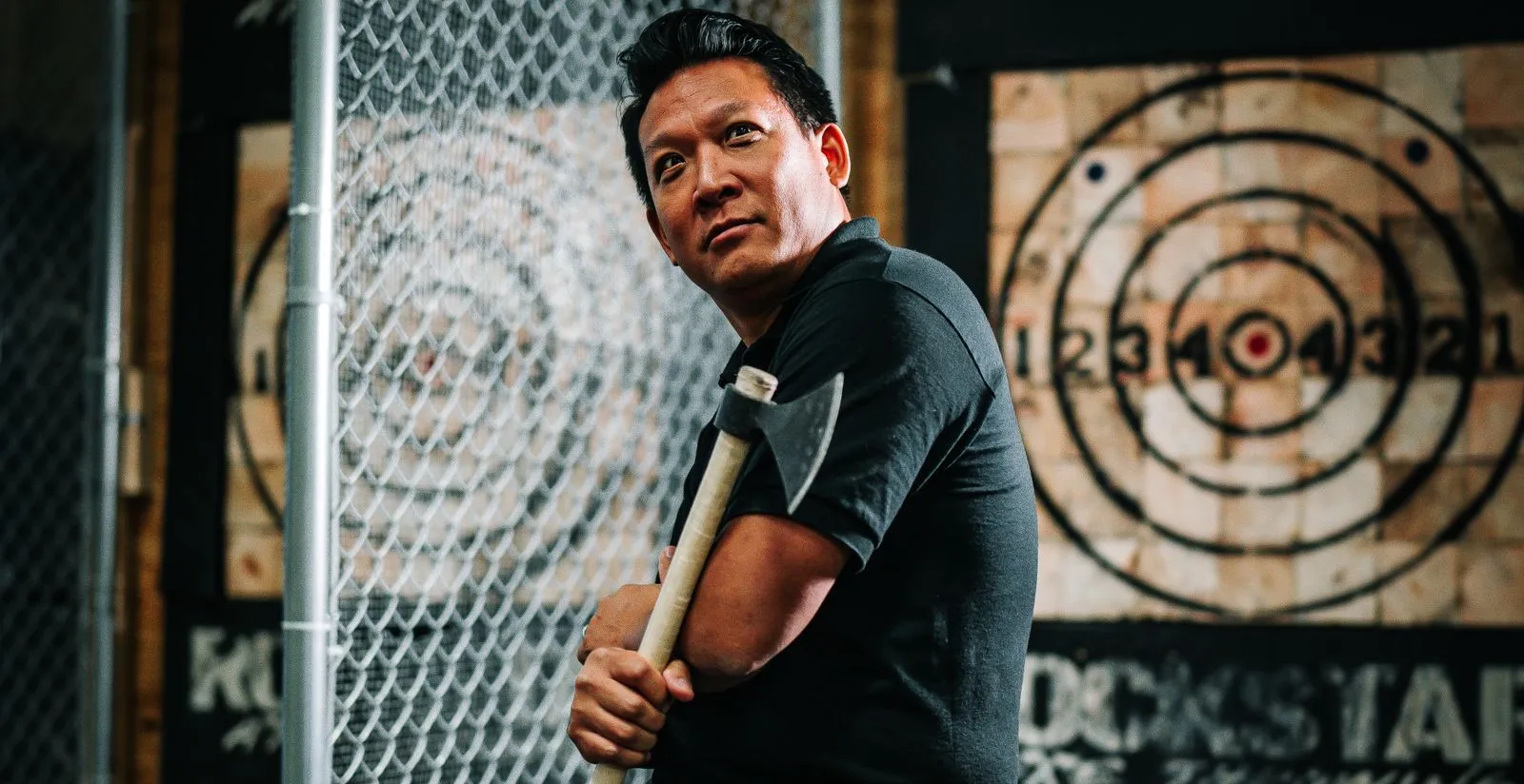 Man posing with an axe in an indoor axe throwing facility, ready for sport.